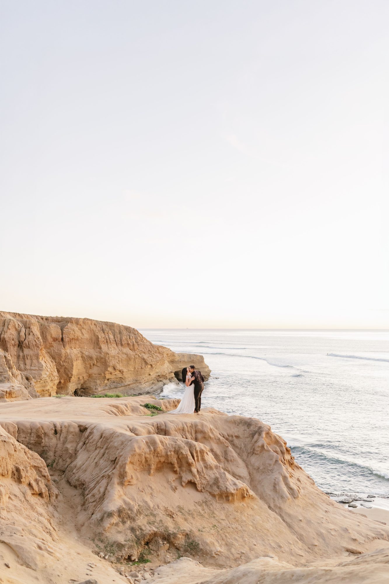 Bride and groom kissing on oceanside cliffs at sunset during a destination wedding portrait session