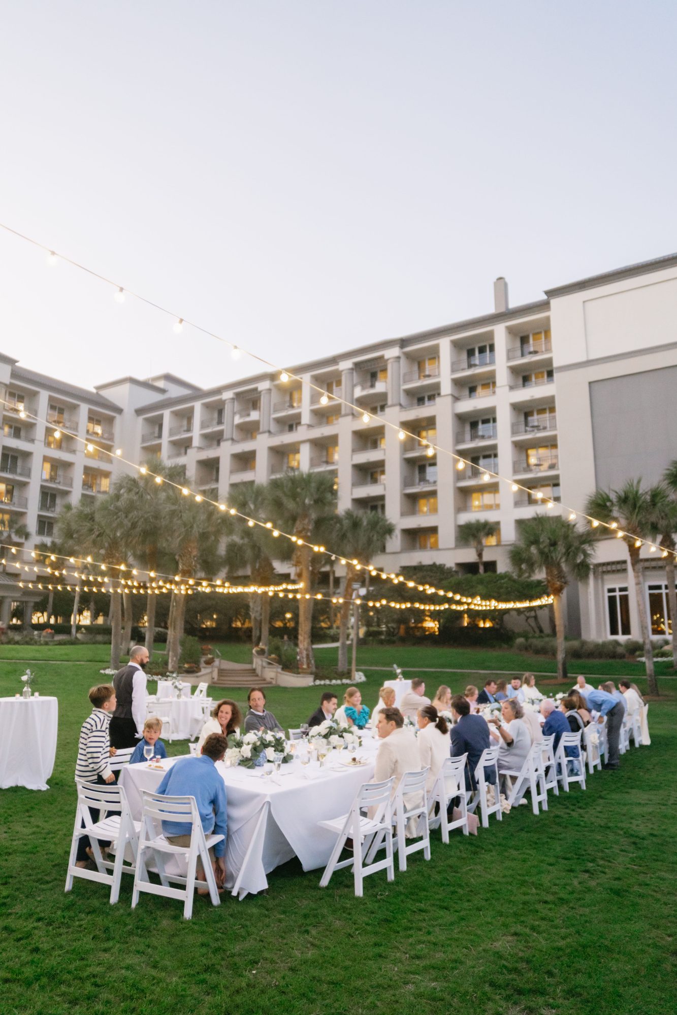 Outdoor destination wedding reception dinner under string lights on a resort lawn