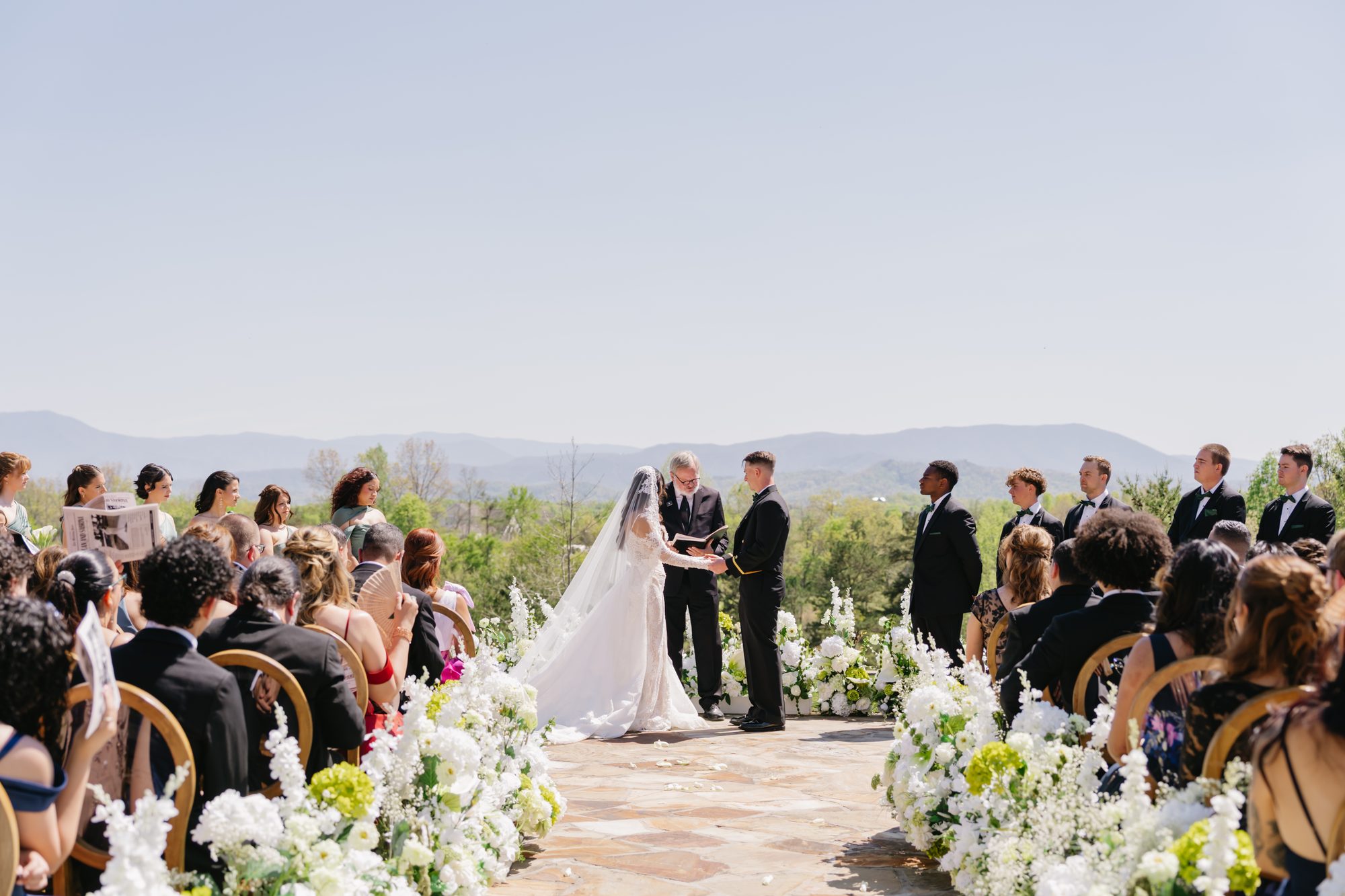 Destination wedding ceremony with mountain views as couple exchanges vows surrounded by white florals