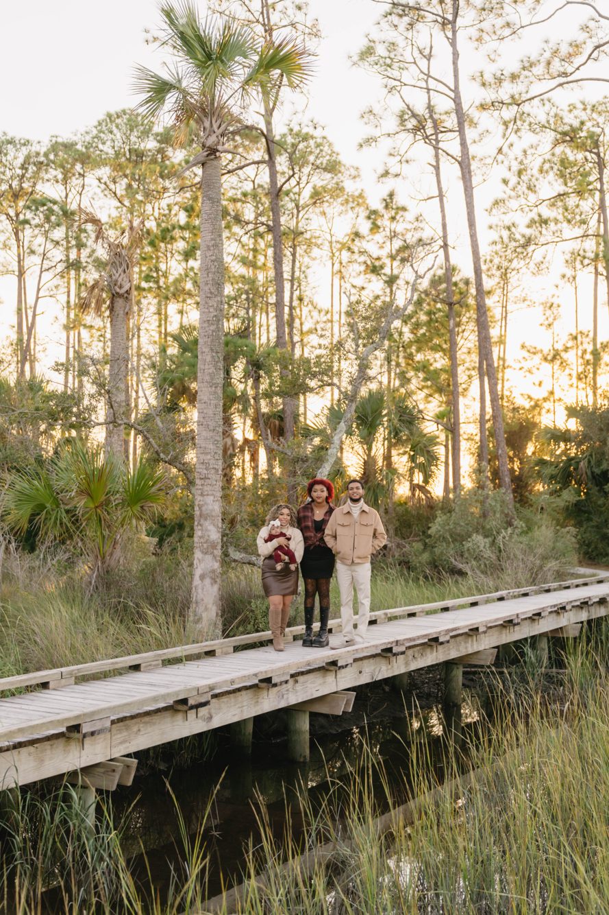 Family with baby on the marsh boardwalk among pines and palms at sunset, Dutton Island Preserve near Mayport