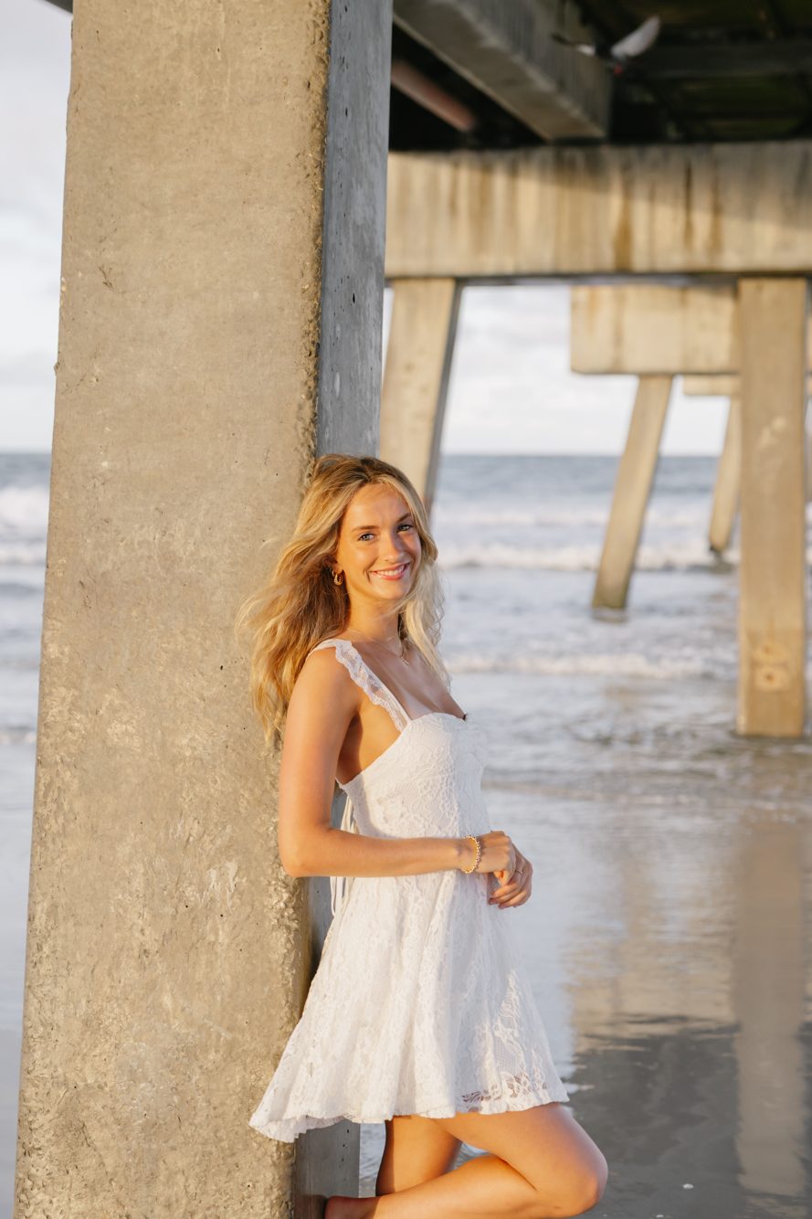 Couple sharing a forehead kiss beneath the pilings of the Jacksonville Beach Pier in golden light by Lee Photo + Video