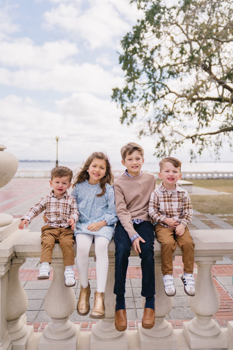 Four siblings sitting on the historic stone balustrade with the St. Johns River behind them at Memorial Park, Jacksonville