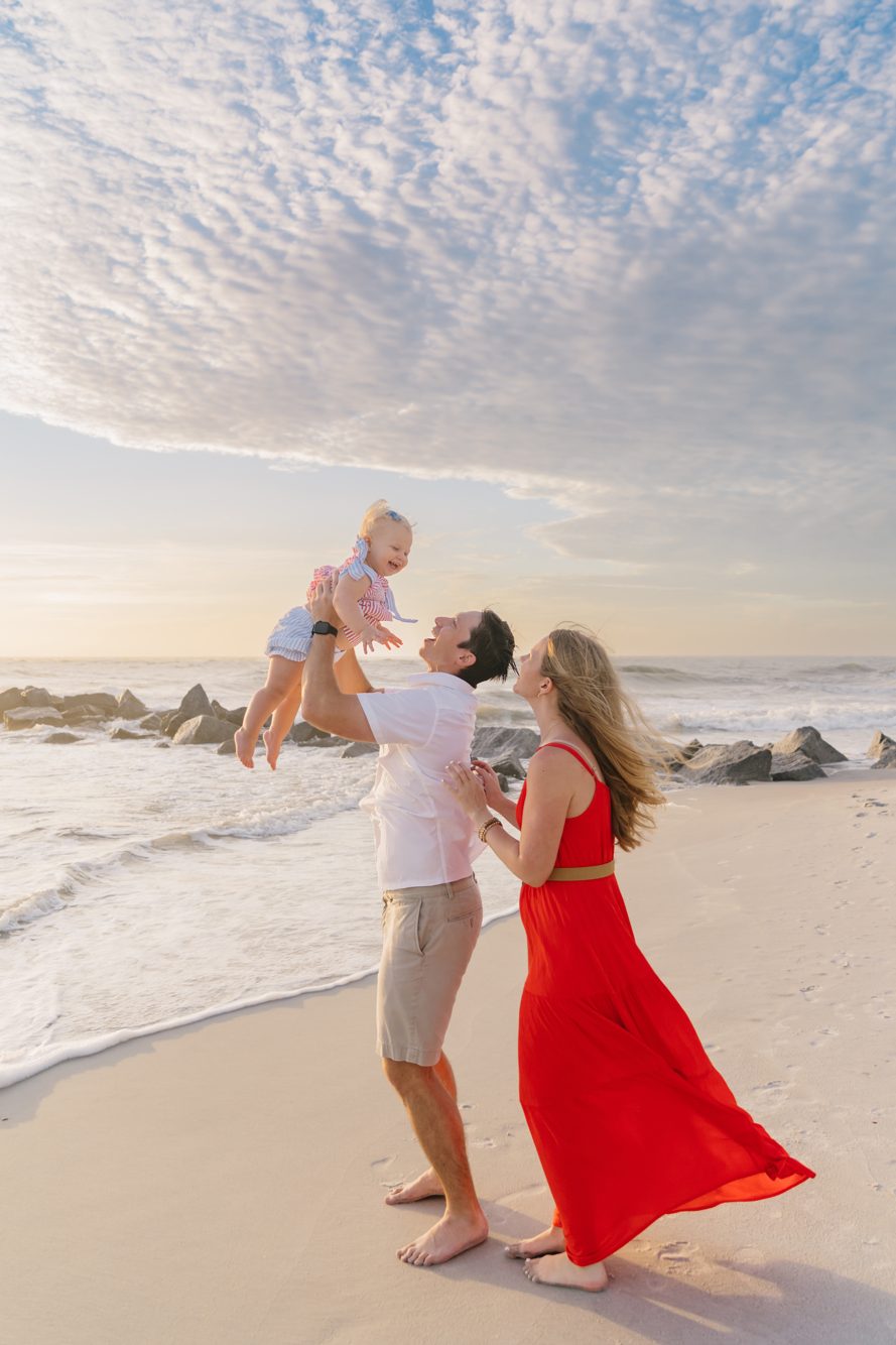 Dad lifting laughing baby with mom by the rocky jetties at Vilano Beach near St. Augustine FL by Lee Photo + Video